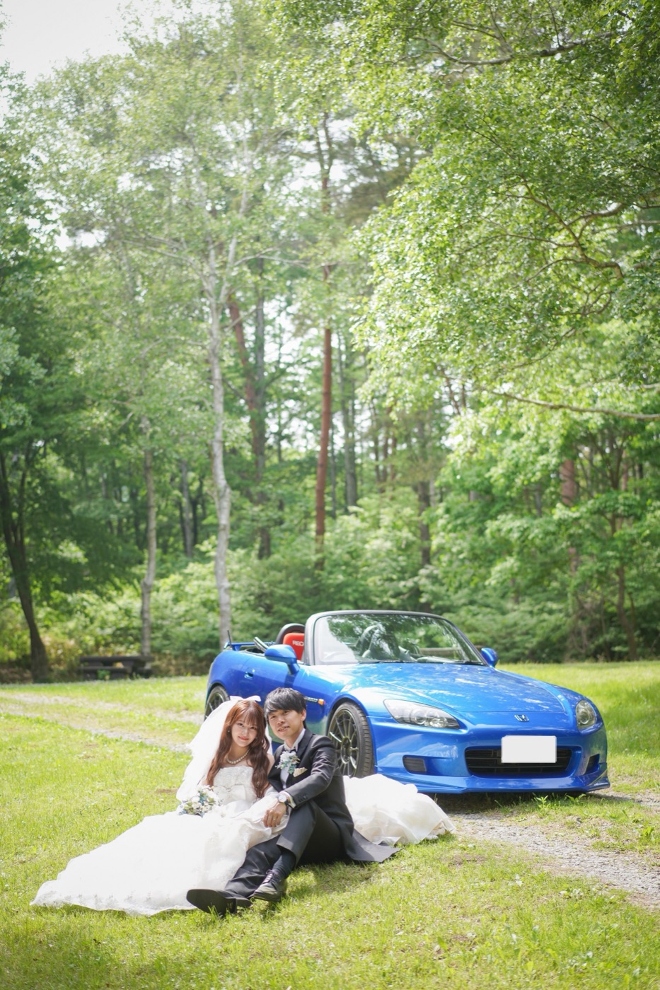 自然の中で青いオープンカーとくつろぐ新郎新婦
